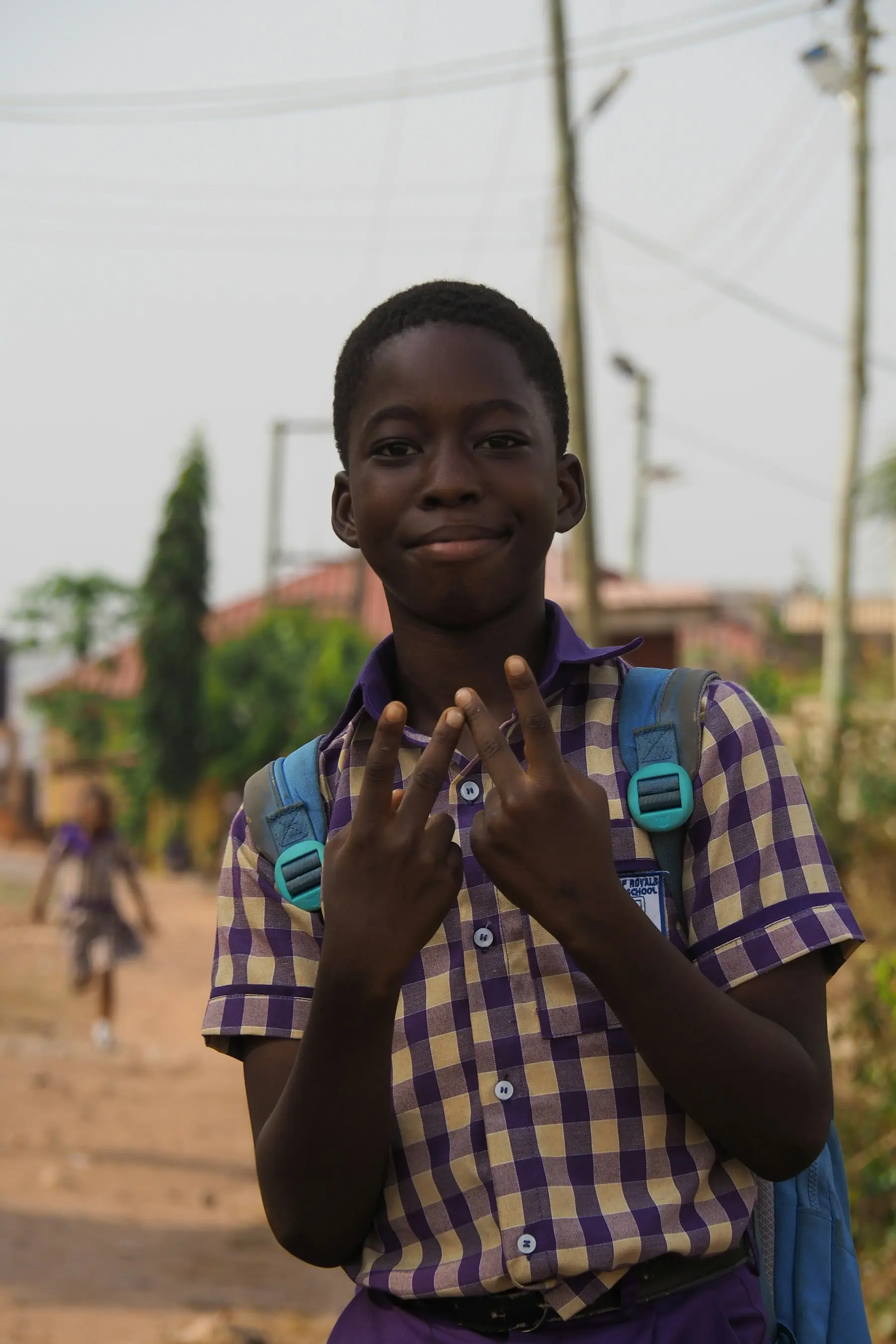 A schoolboy in uniform flashing peace signs on his way to school
